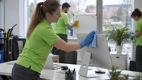 Addetta alle pulizie pulisce lo schermo di una postazione d’ufficio