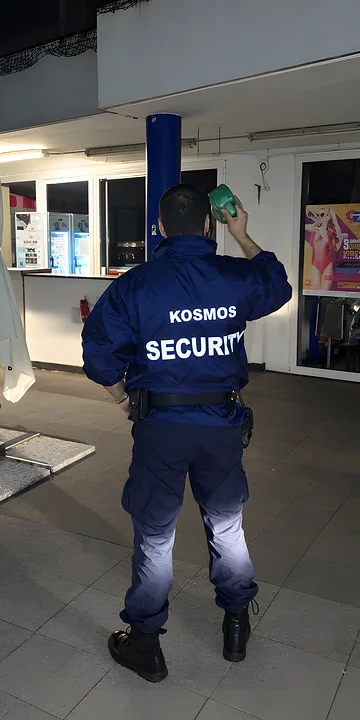Addetto Kosmos Security, di spalle, durante un turno di guardiania notturna davanti a un edificio commerciale
