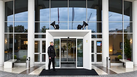 Operatore Kosmos Security davanti all’ingresso vetrato di un edificio commerciale