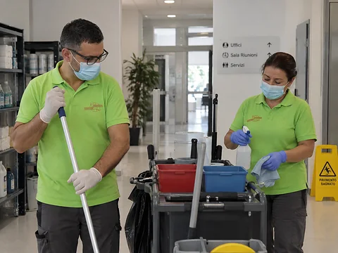 Due addetti Kosmos con mascherina e guanti durante la sanificazione di un corridoio di uffici